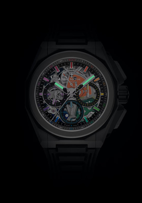 A close-up of the Zenith Defy Extreme Chroma luxury watch, featuring a microblasted titanium case and band, a transparent dial revealing colorful El Primero 9004 movement, and glowing green hands.