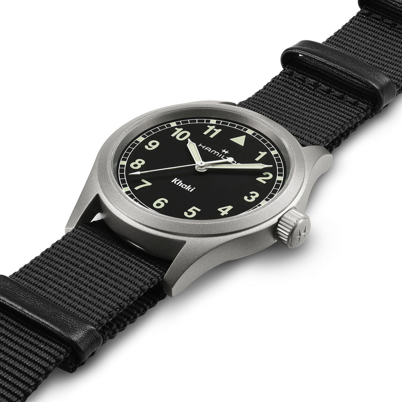 The Hamilton Khaki Field Quartz features white numerals on a black dial with a black nylon strap, shown at an angle on a white background.