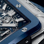 Close-up of the Hublot Square Bang Unico Titanium Blue Ceramic, featuring a blue ceramic bezel, exposed gears, silver hour markers, and intricate mechanics under a sapphire crystal dial.