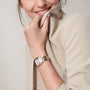 A person in a light beige blazer smiles while holding the collar, wearing the Panthère de Cartier watch by Cartier—a two-tone metal timepiece with a square white face, Roman numerals, and 18K yellow gold accents.