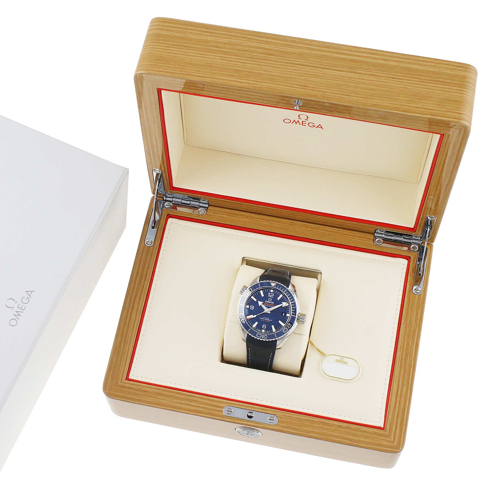An OMEGA Seamaster Planet Ocean 600M wristwatch with a black strap is shown in an open wooden presentation box beside a white OMEGA-branded box.