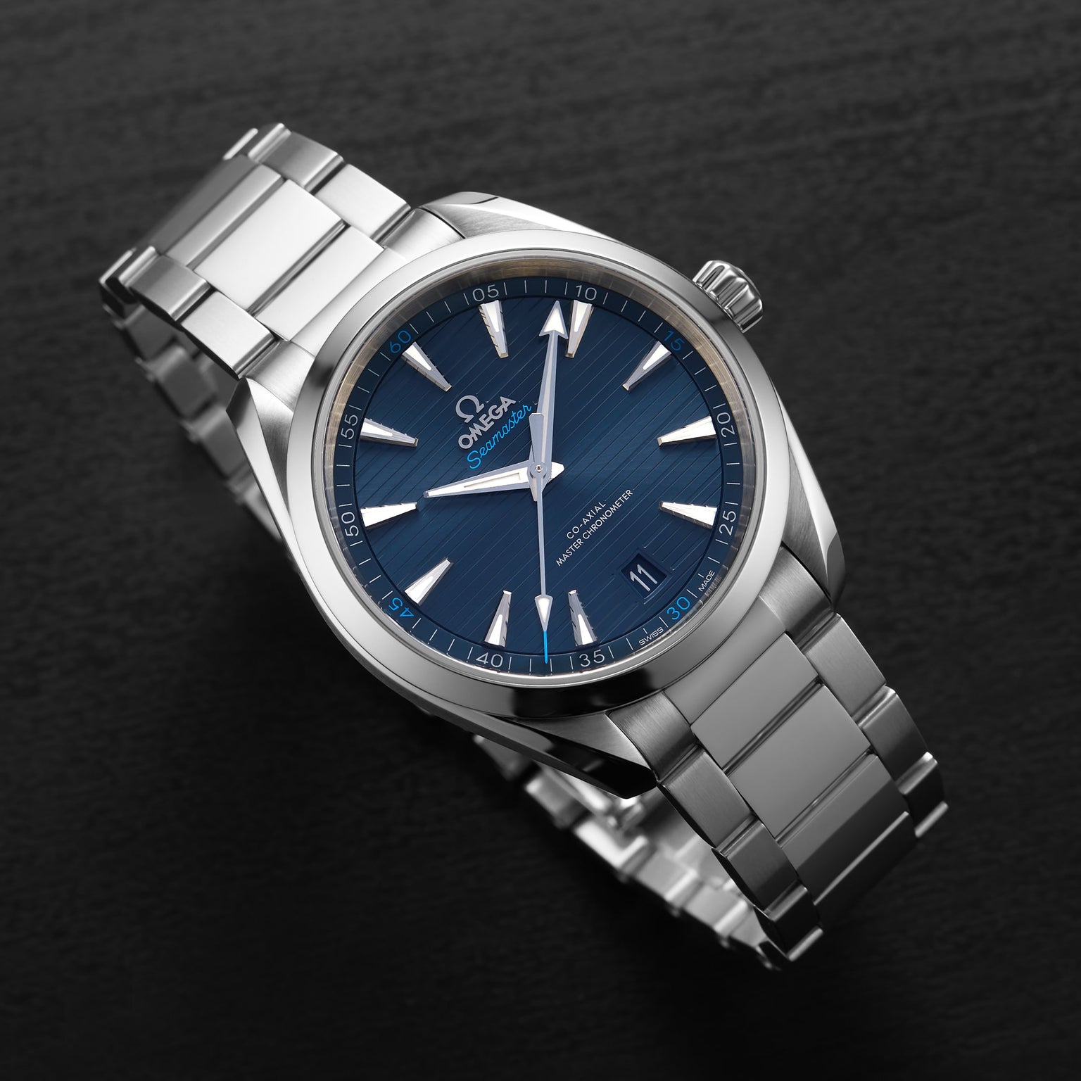 An OMEGA Seamaster Aqua Terra 150M wristwatch with a blue dial, silver hour markers, and stainless steel bracelet is shown on a black surface.