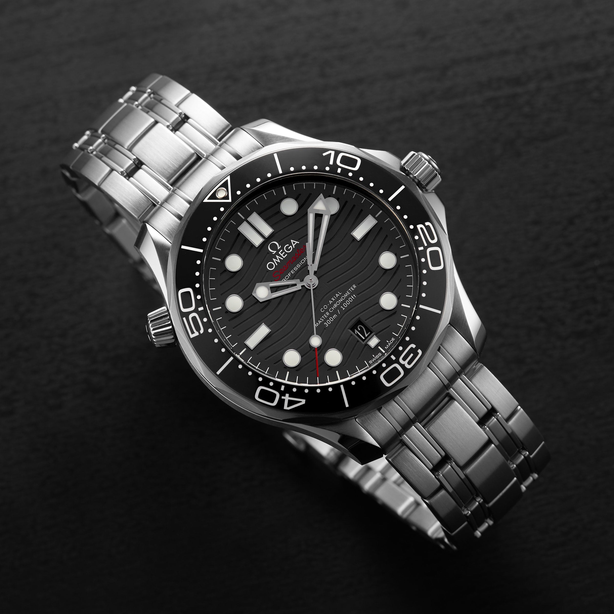 An OMEGA Seamaster Diver 300M wristwatch with a stainless steel bracelet, black dial, and white markers is displayed on a dark surface.