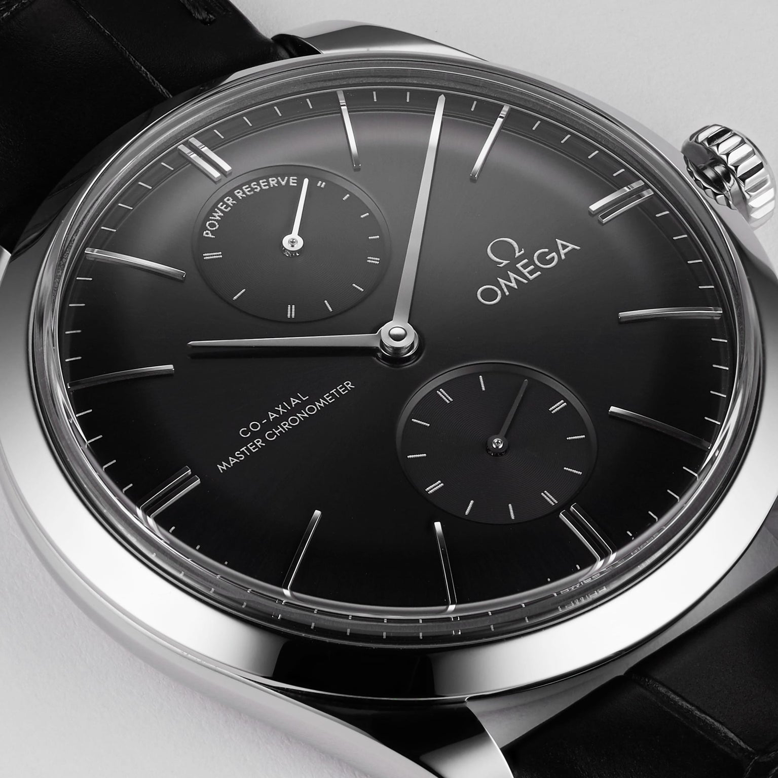 Close-up of an OMEGA De Ville Trésor featuring a 40mm stainless steel case, black dial with two subdials, silver markers, black leather strap, and the text “Co-Axial Master Chronometer” and “Power Reserve.”.
