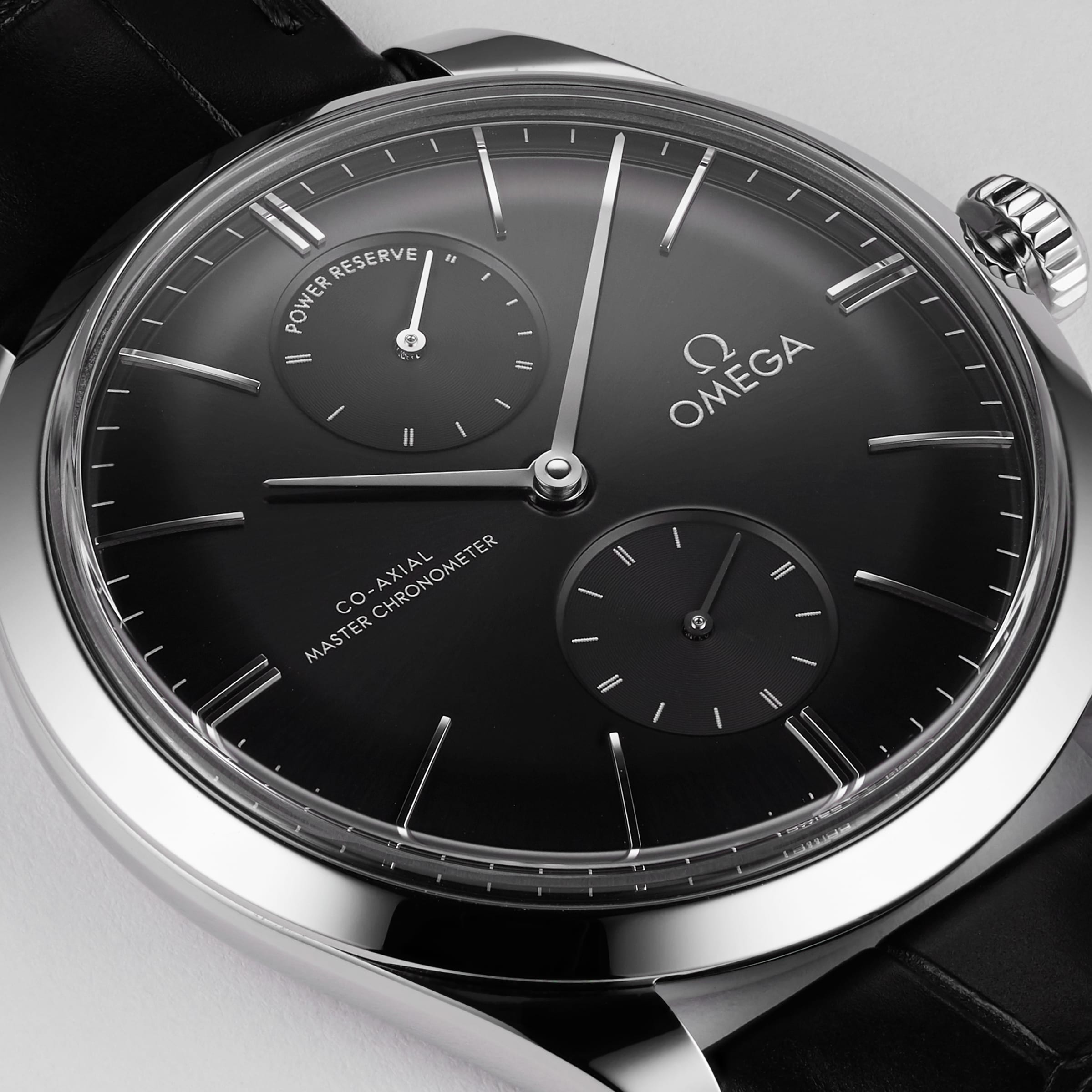 Close-up of an OMEGA De Ville Trésor featuring a 40mm stainless steel case, black dial with two subdials, silver markers, black leather strap, and the text “Co-Axial Master Chronometer” and “Power Reserve.”.