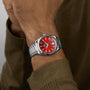 Someone wearing an OMEGA Seamaster Aqua Terra 150M with a silver case, red dial, date display, and precise 8800 calibre movement, paired with a greenish-brown long sleeve shirt.