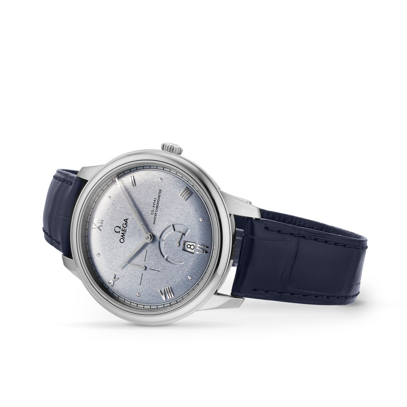 The OMEGA De Ville Prestige wristwatch features a blue leather strap, Roman numerals, date display, and stainless steel case. Angled on a white background, this model epitomizes Master Chronometer elegance.