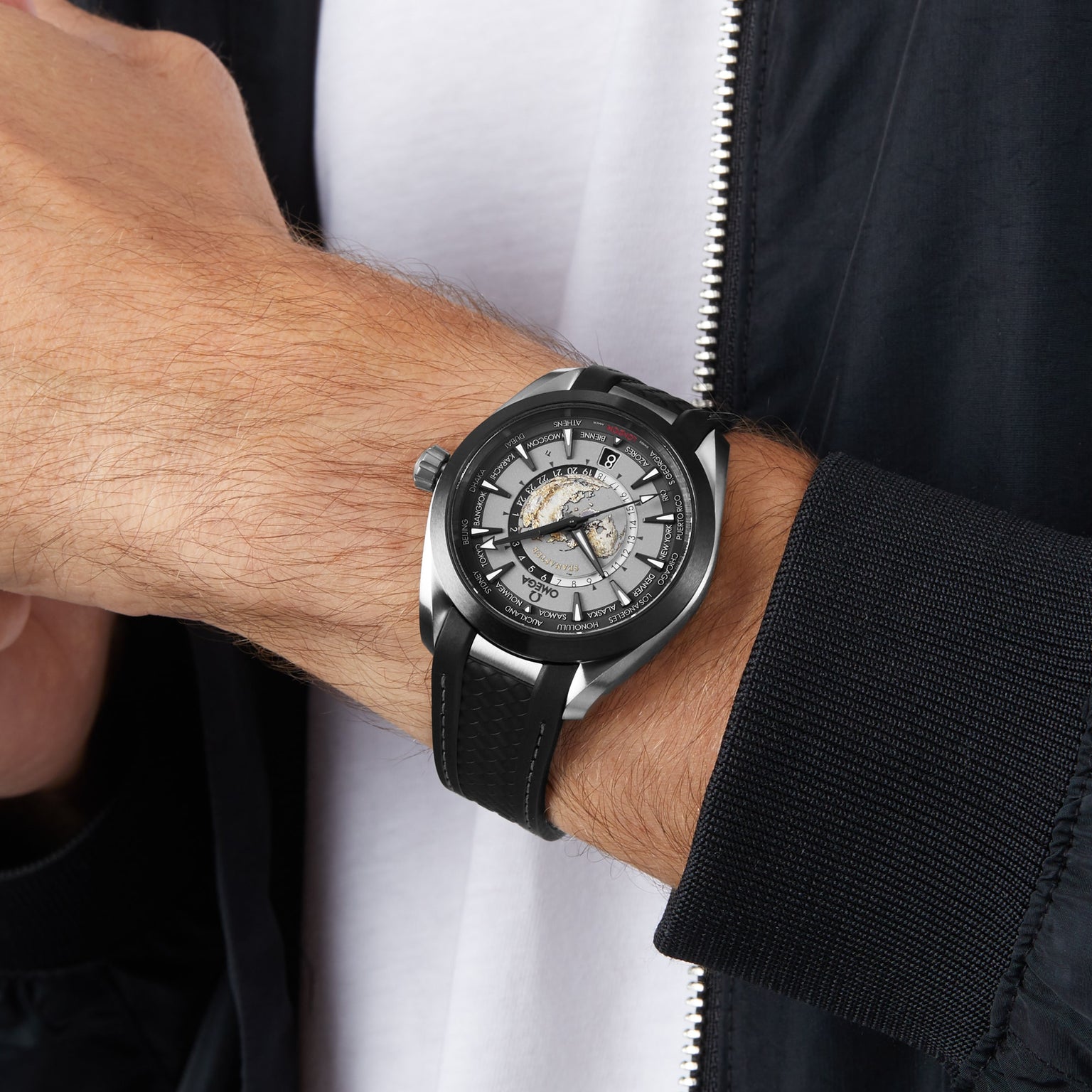 A person in a black jacket and white shirt wears the OMEGA Seamaster Aqua Terra 150M, featuring a silver and black wristwatch with a detailed, partially exposed mechanical dial in a sleek titanium case.