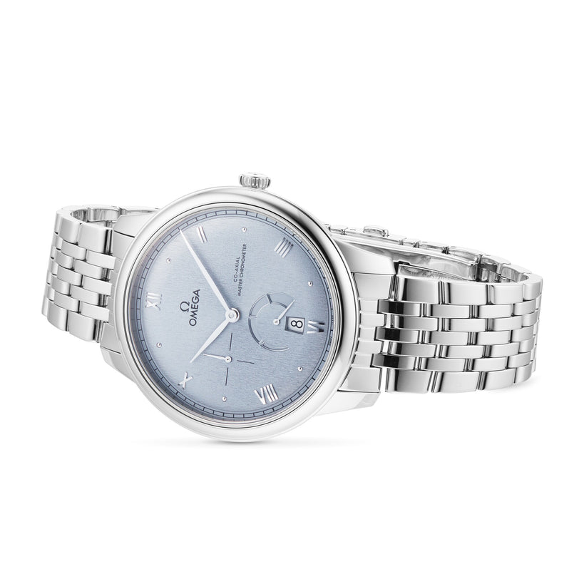 The OMEGA De Ville Prestige, featuring a silver case, blue dial with Roman numerals, date at 3 o’clock, and metal bracelet band, is displayed against a white background to highlight its classic design.