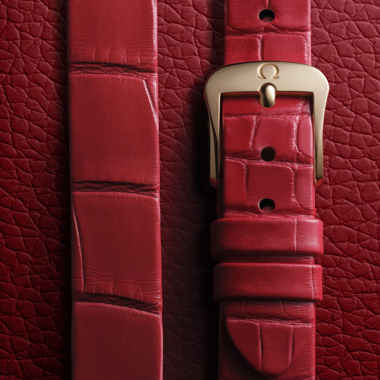 Close-up of the OMEGA De Ville Mini Trésors red leather strap with a gold buckle, set on textured red leather, highlighting its elegant design and signature 18K Moonshine™ Gold detailing.