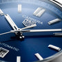 Close-up of a blue TAG Heuer Carrera Date watch face, featuring hands, hour markers, logo, and partial date window.