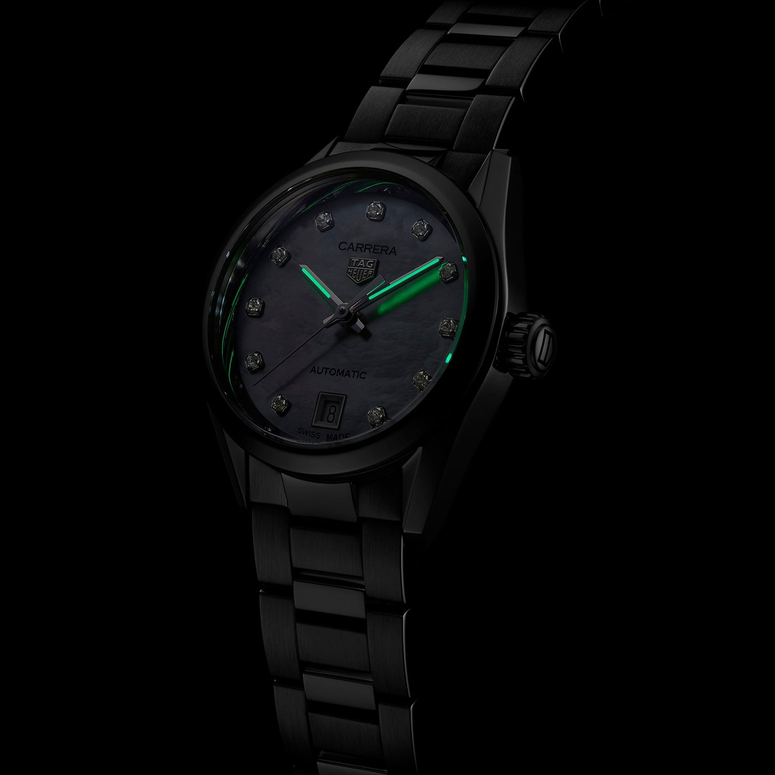 The TAG Heuer Carrera Date is a black metal wristwatch with a dark face, diamond hour markers, date display, and green luminescent hour and minute hands.