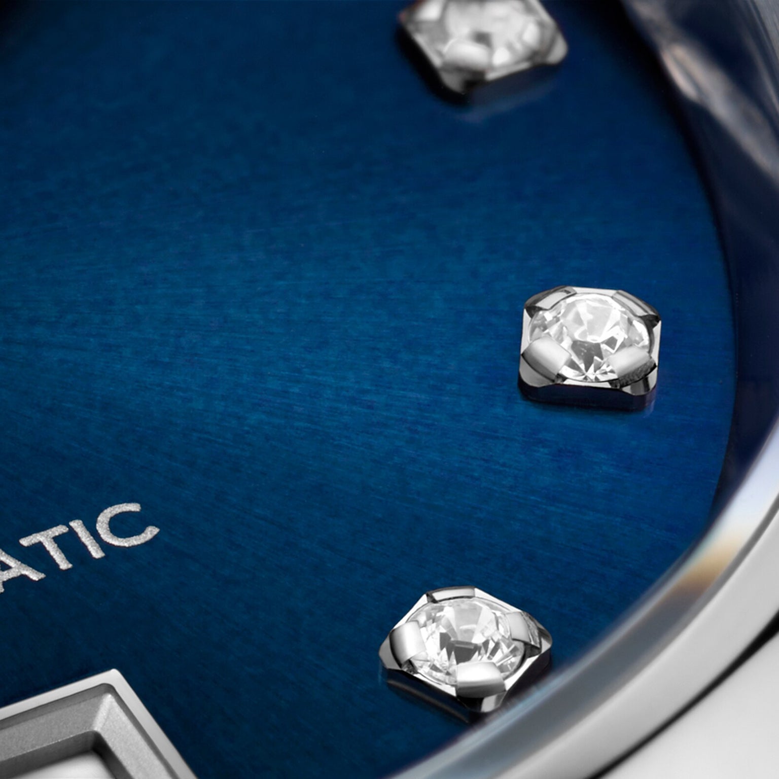 Close-up of the TAG Heuer Carrera Date watch, showcasing a blue sunray dial with diamond hour markers and a partial view of the silver AUTOMATIC inscription.