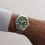 A person wears a TAG Heuer Aquaracer Professional 300 Date with a green bezel and dial, showing 10:10. The stainless steel watch sits on their left wrist over a light gray sleeve.