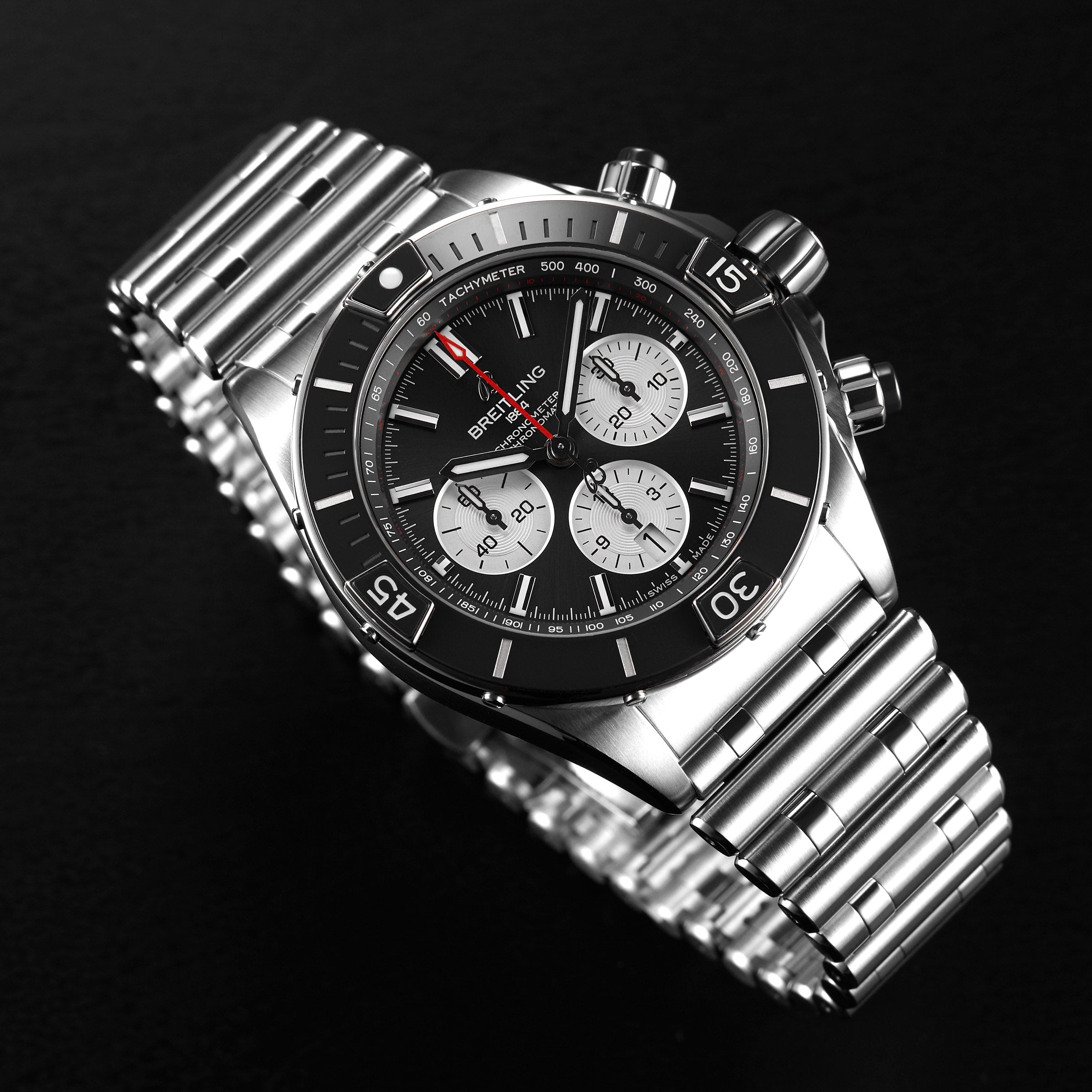 The Breitling Super Chronomat B01 44, featuring a stainless steel case, black dial with three subdials, tachymeter scale, and Rouleaux bracelet, is displayed against a black background.