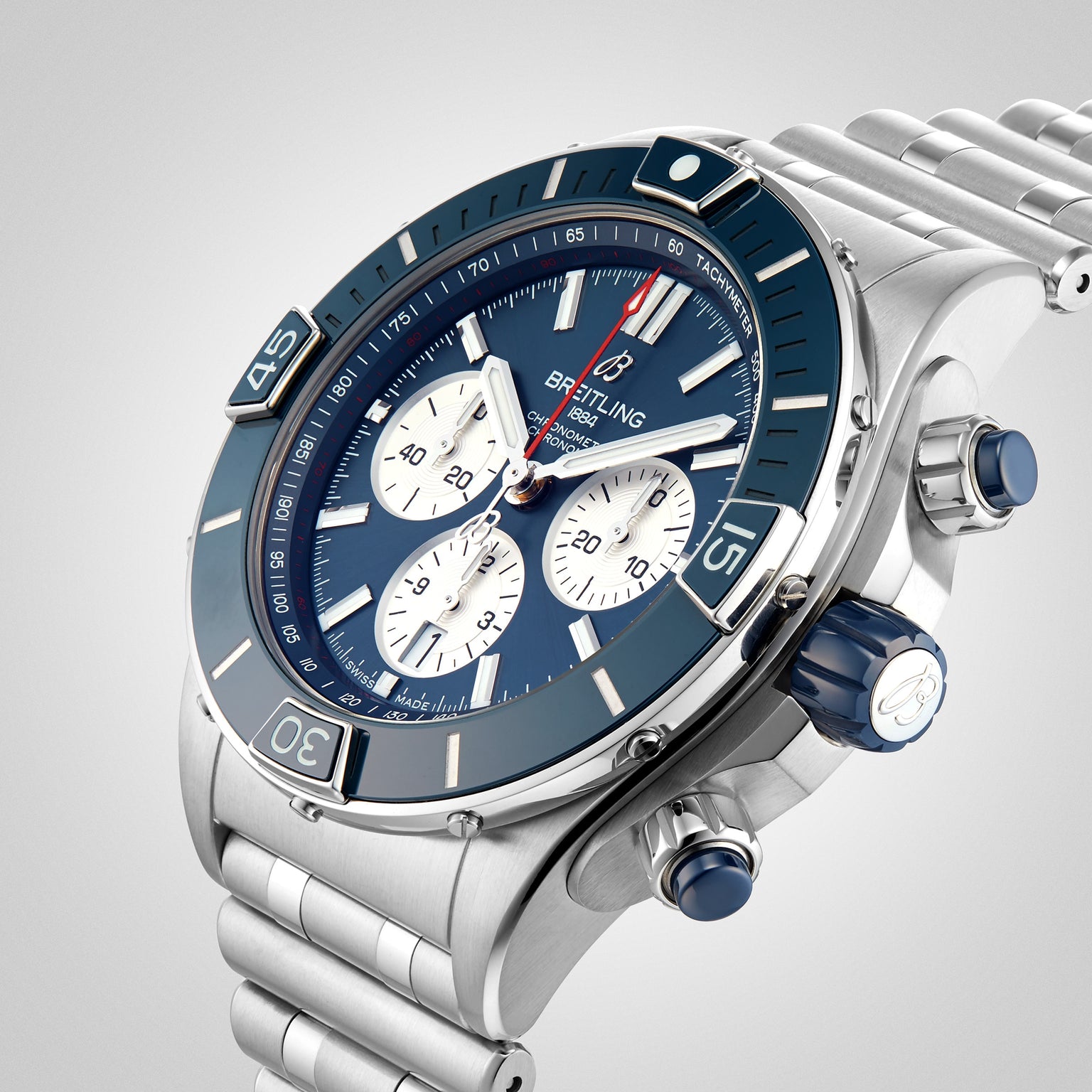 The Breitling Super Chronomat B01 44 is a stainless steel mechanical chronograph watch with a blue bezel and dial, three subdials, and a metal link bracelet, shown against a light background.