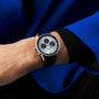 Wearing a blue and black jacket, a person shows off a Breitling Navitimer B01 Chronograph 43 with a white and black dial and black leather strap on their left wrist.