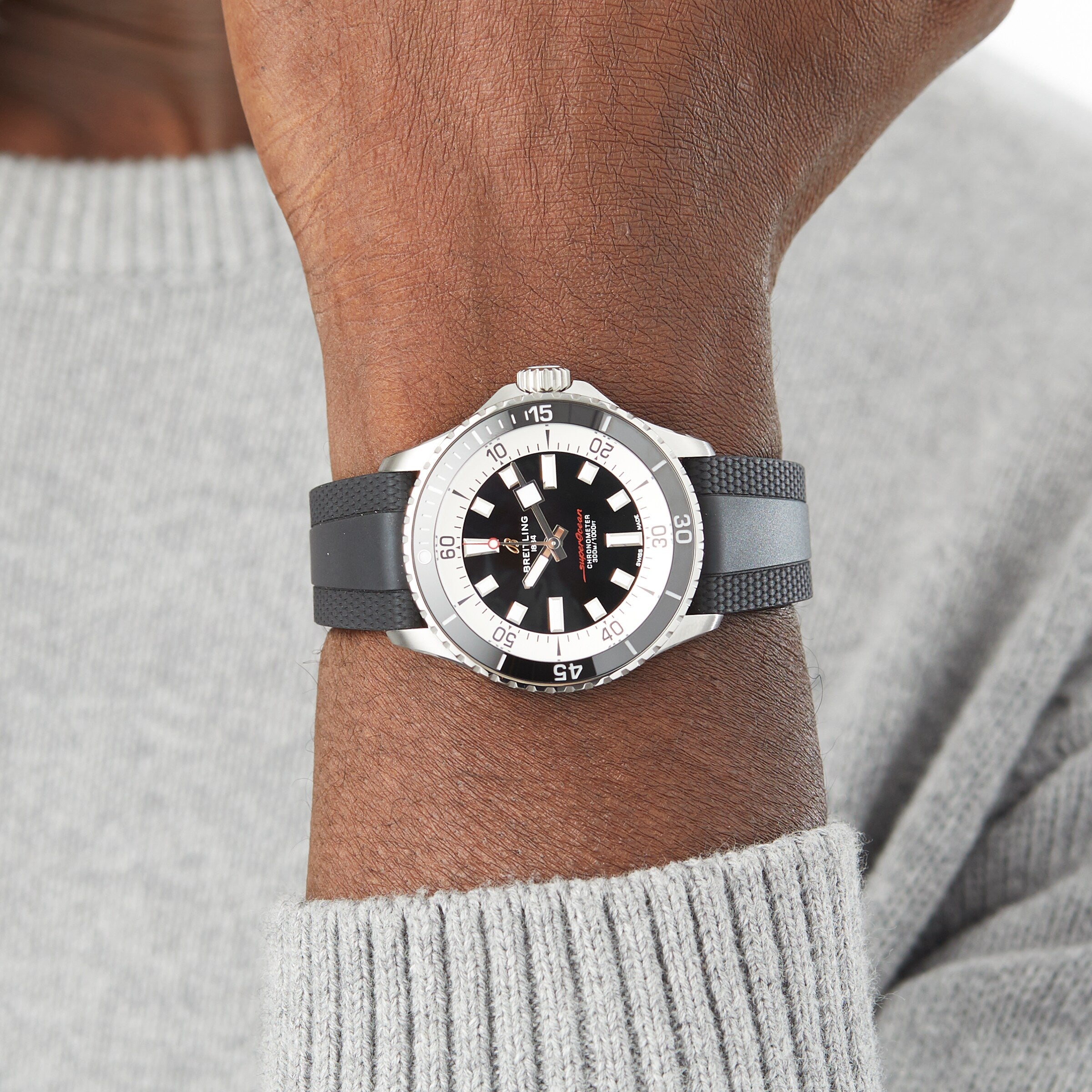 A person wearing a Breitling Superocean Automatic 42 with a black rubber strap and a gray knit sweater.