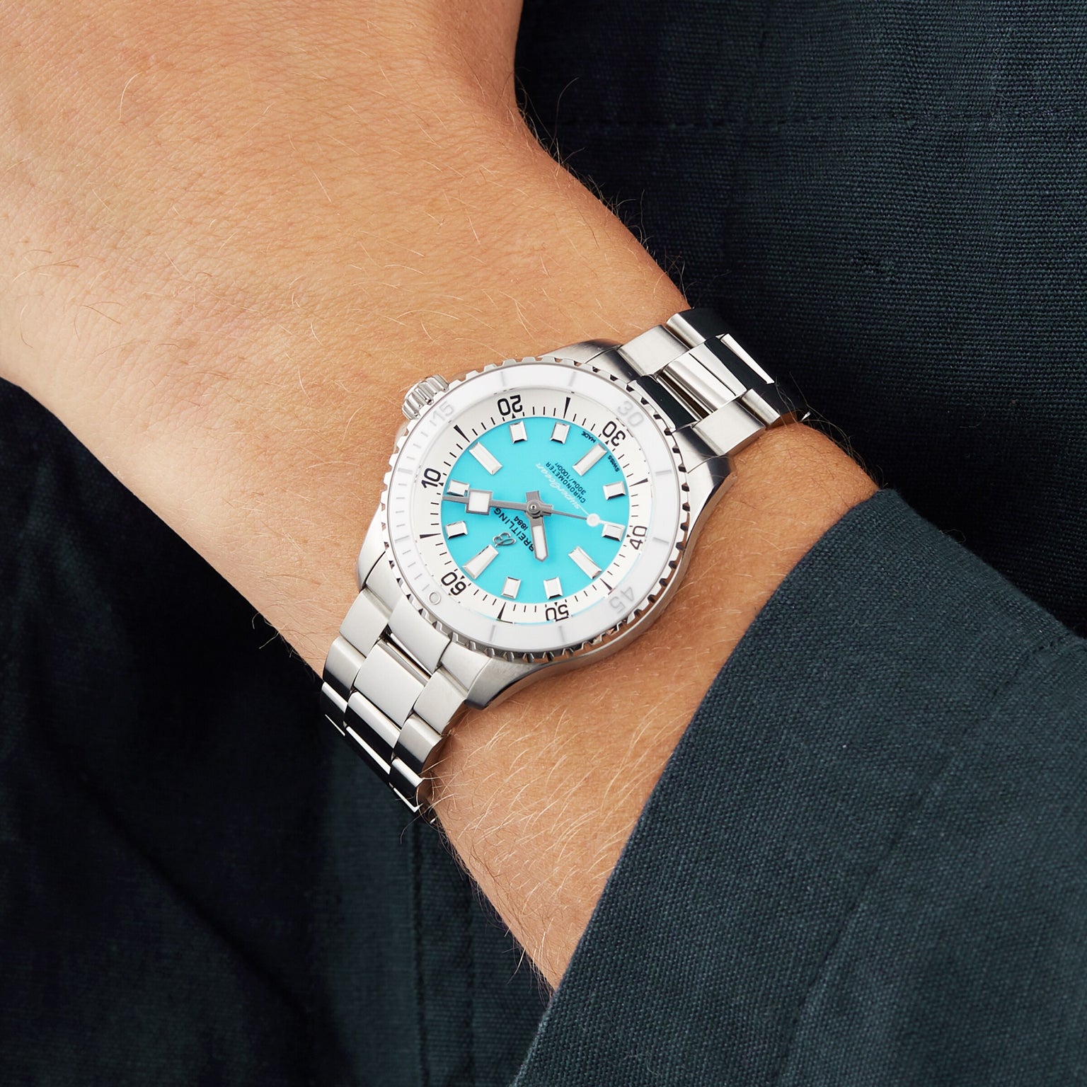 A person wears a Breitling Superocean Automatic 36 diving watch with a silver case, turquoise dial, and silver markers, paired with a dark long-sleeve shirt.