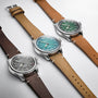 Three Oris Big Crown Oris X Cervo Volante watches with leather straps are shown side by side, each with a stainless steel case, large numerals, and gray, teal, or green dials that showcase the classic style of the series.