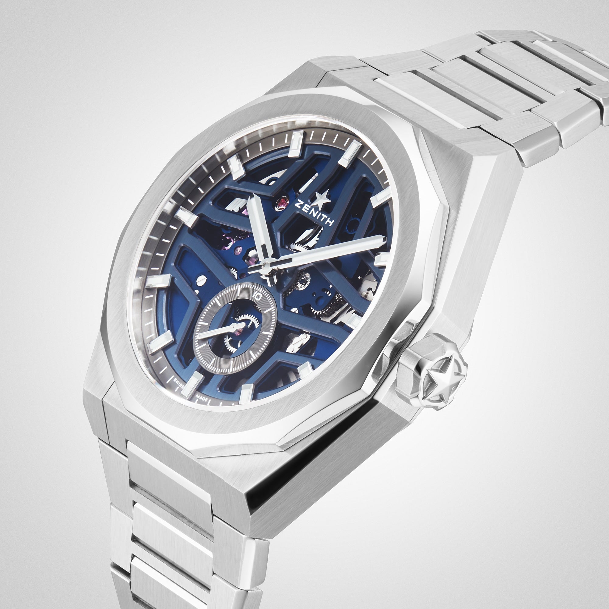The Zenith Defy Skyline Skeleton wristwatch, featuring a blue skeleton dial with exposed gears and a stainless steel bracelet, embodies urban sophistication against a light backdrop.