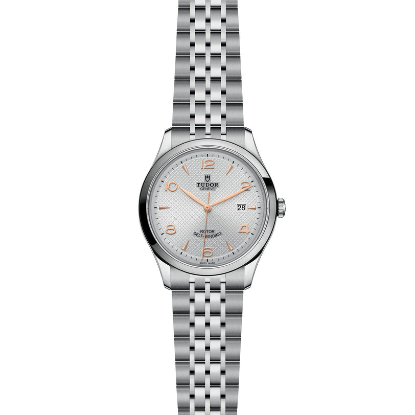 The TUDOR 1926 is a silver wristwatch featuring a metal link bracelet, white dial, gold-tone hour markers and hands, self-winding movement, and a date display at 3 o’clock.