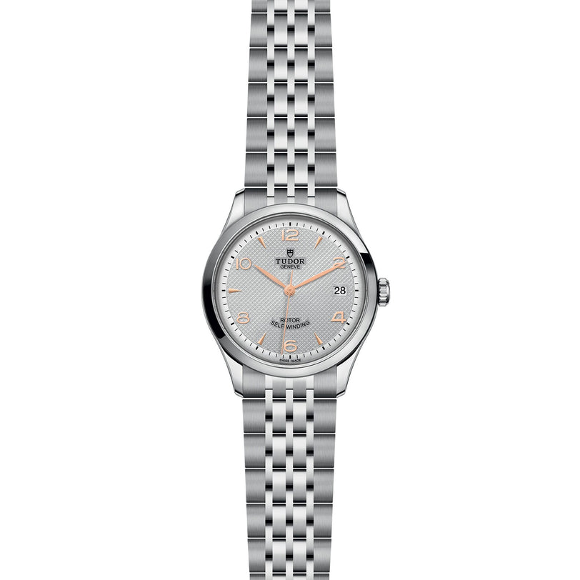 A silver TUDOR 1926 wristwatch featuring a white dial, gold hour markers, date at 3 o’clock, and a metal link bracelet—a refined showcase of TUDOR’s expert mechanical watchmaking.