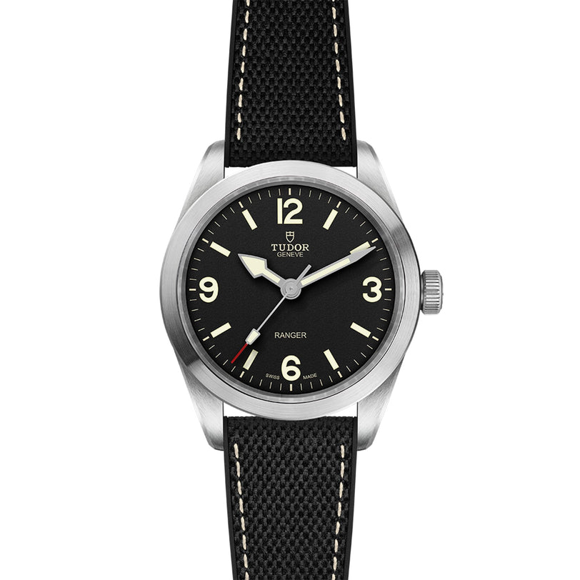 The TUDOR Ranger wristwatch features a black dial with Super Luminova numerals at 12, 3, 6, and 9, a silver case, and a black textured strap with white stitching.
