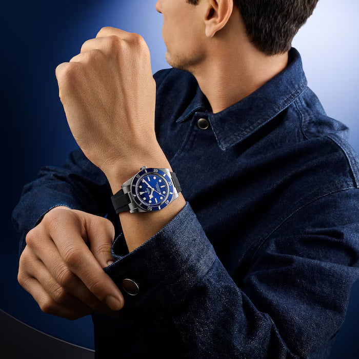 Man wearing dark denim shirt with Black Bay 54 watch featuring blue dial and black rubber strap.