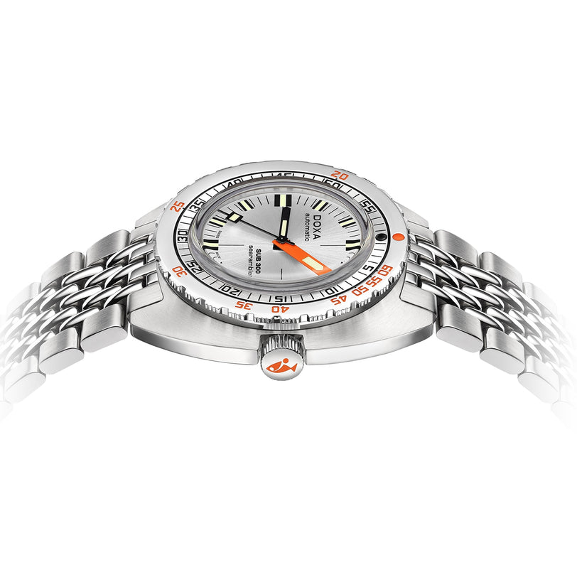 The DOXA Sub 300 Searambler, a stainless steel divers watch with a silver dial, orange accents, and metal bracelet, features a unidirectional bezel and is shown from a low side angle against a white background.