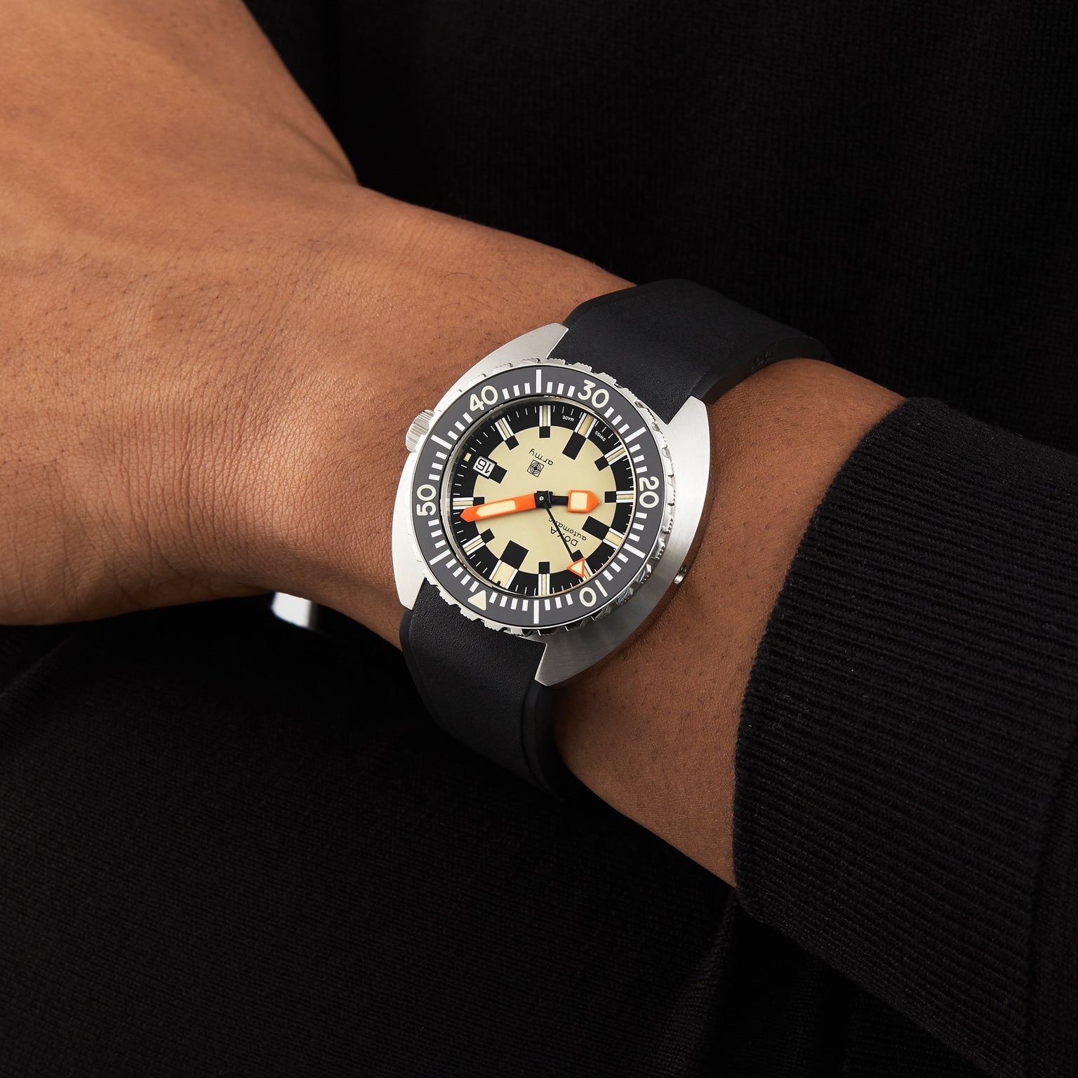A person wearing a black long-sleeve shirt and a DOXA Army Stainless Steel watch by DOXA, featuring a cream dial with bold black and orange accents plus Super-LumiNova® coating for enhanced readability.