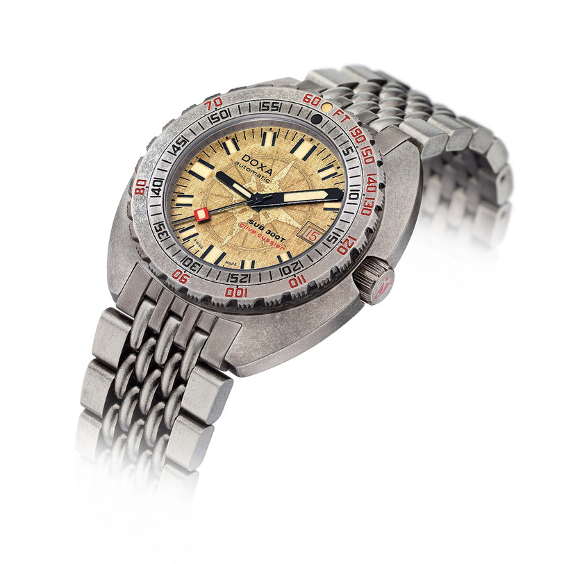 The DOXA Sub 300T Clive Cussler wristwatch features a textured gold dial with black and red markers, a metal link bracelet, Swiss automatic movement, and water resistance up to 1200 meters.