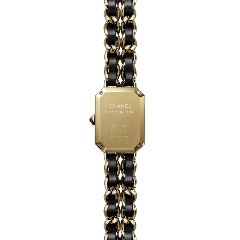A close-up of the back of the Chanel Première Édition Originale Small Model, a rectangular yellow gold steel wristwatch with a black and gold chain-link band, engraved with CHANEL ÉDITION ORIGINALE and other details.