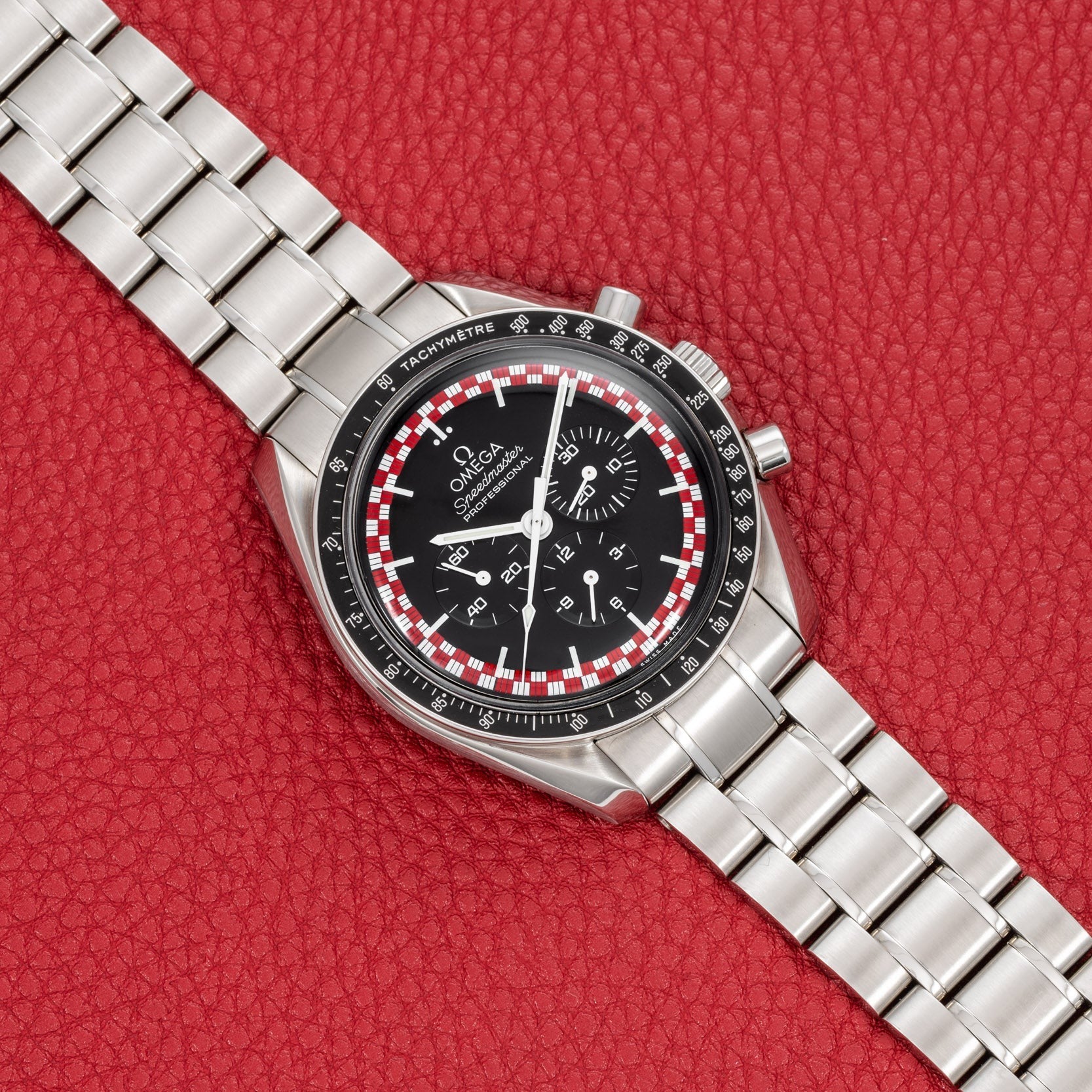 An OMEGA Speedmaster Tintin watch with a black dial and silver case displayed on a red textured background.
