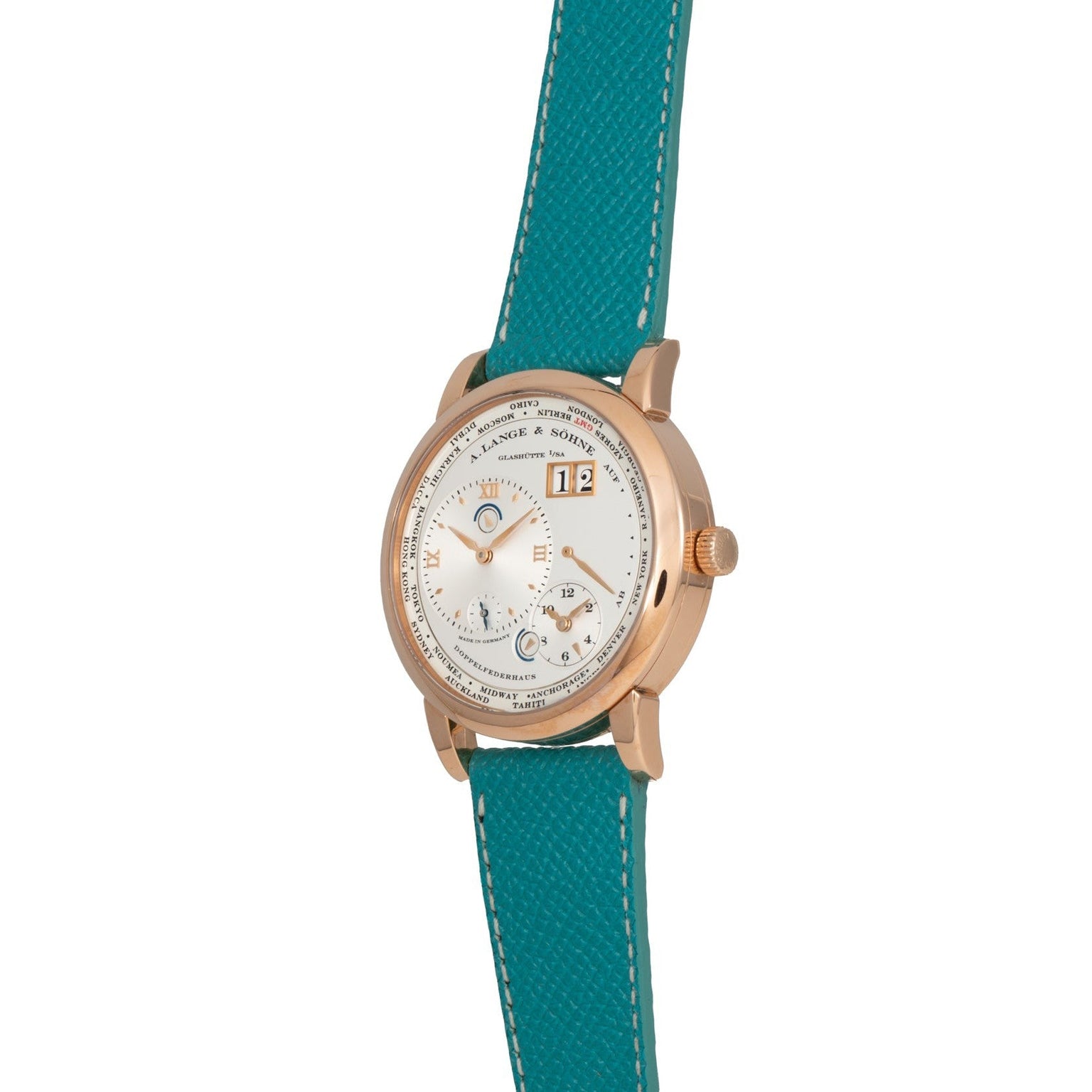 The Lange & Sohne Lange 1 Timezone is a gold watch with a white dial and teal leather strap, featuring multiple subdials and a date window.