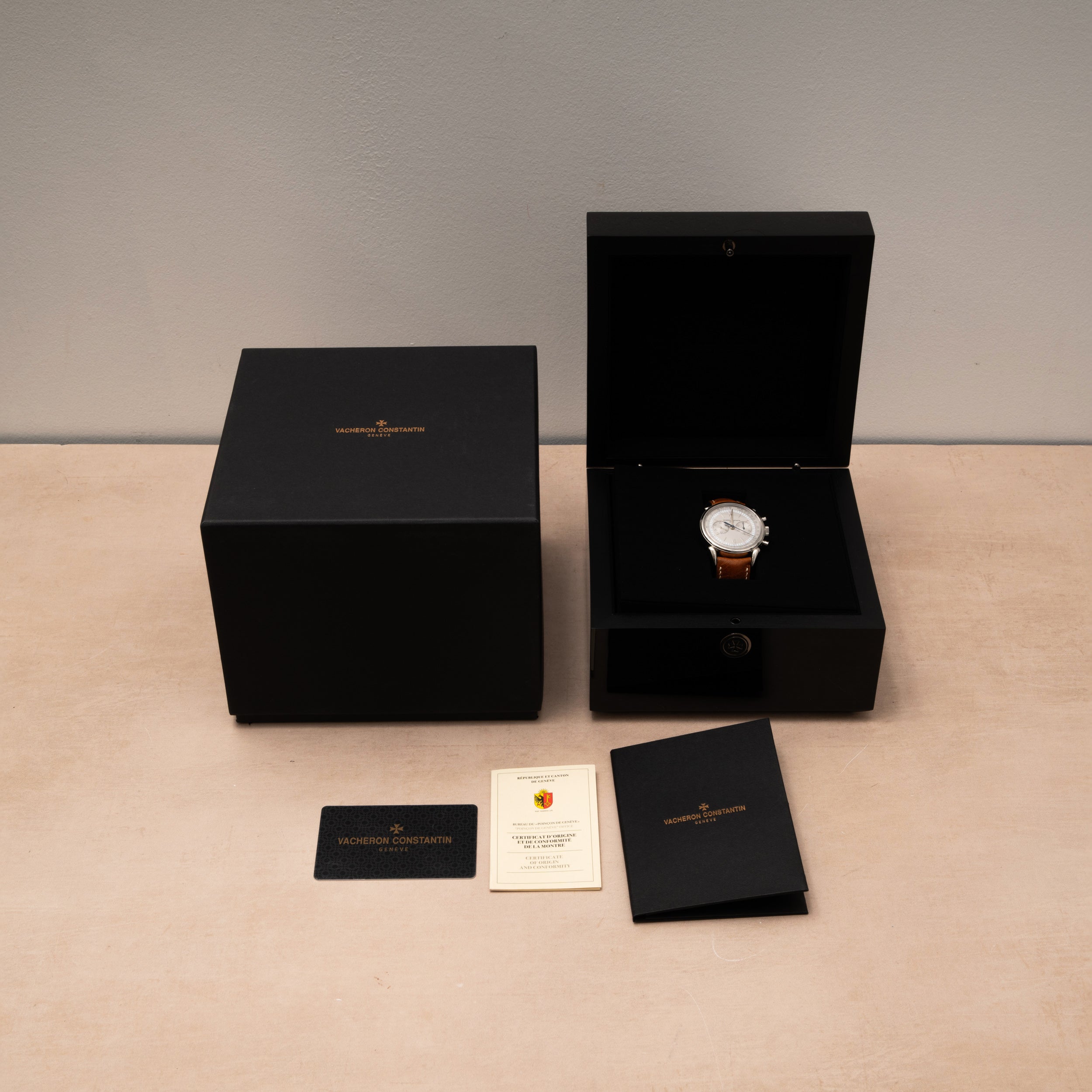 The Vacheron Constantin Historiques Cornes De Vache Chronograph is presented in a black box with documents and cards, elegantly displayed on a beige surface.