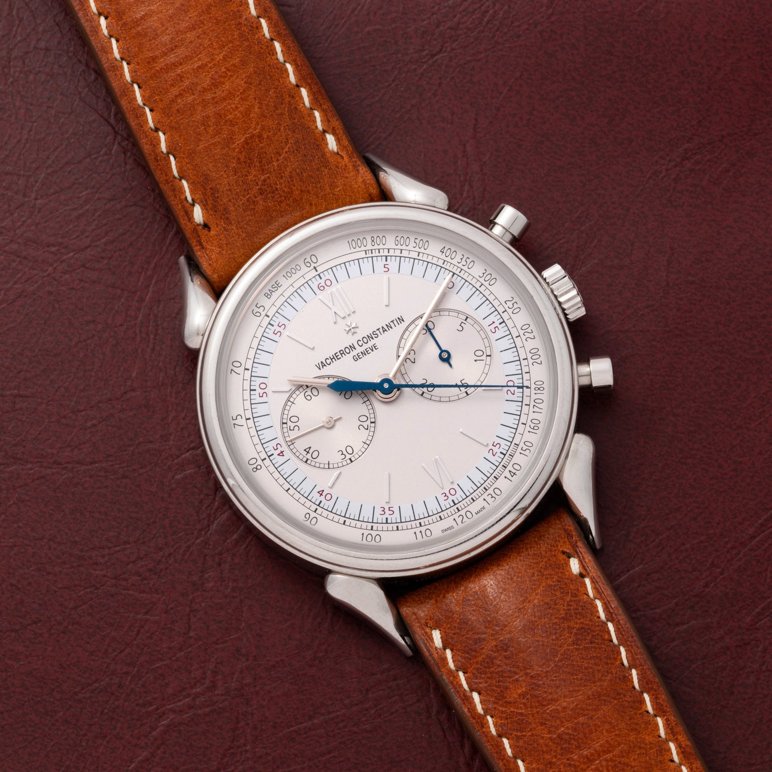 The Vacheron Constantin Historiques Cornes De Vache Chronograph, featuring a silver case and brown leather strap, rests elegantly on a dark brown leather surface.