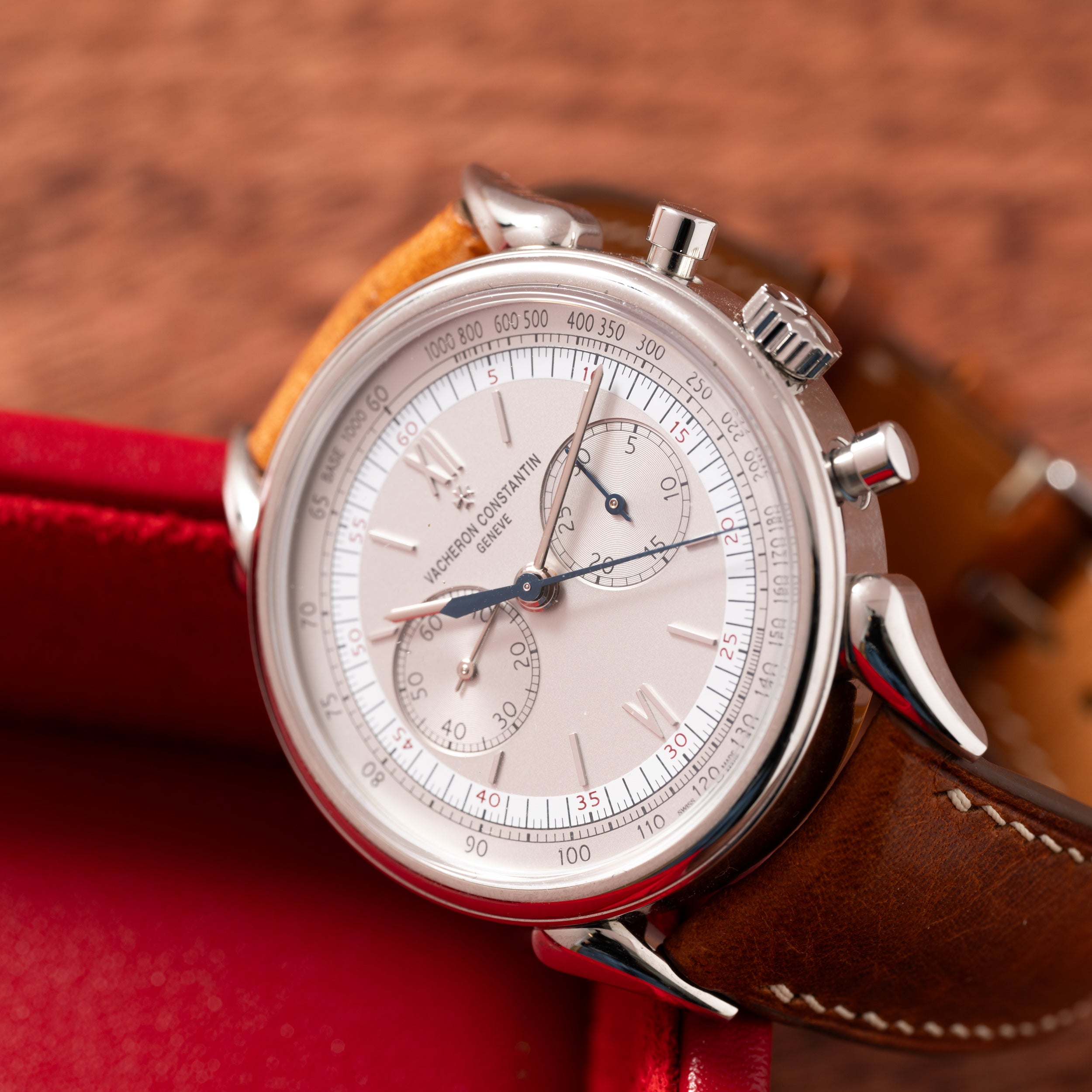 The Vacheron Constantin Historiques Cornes De Vache Chronograph, a luxury watch with a brown leather strap, displayed on a wooden surface.
