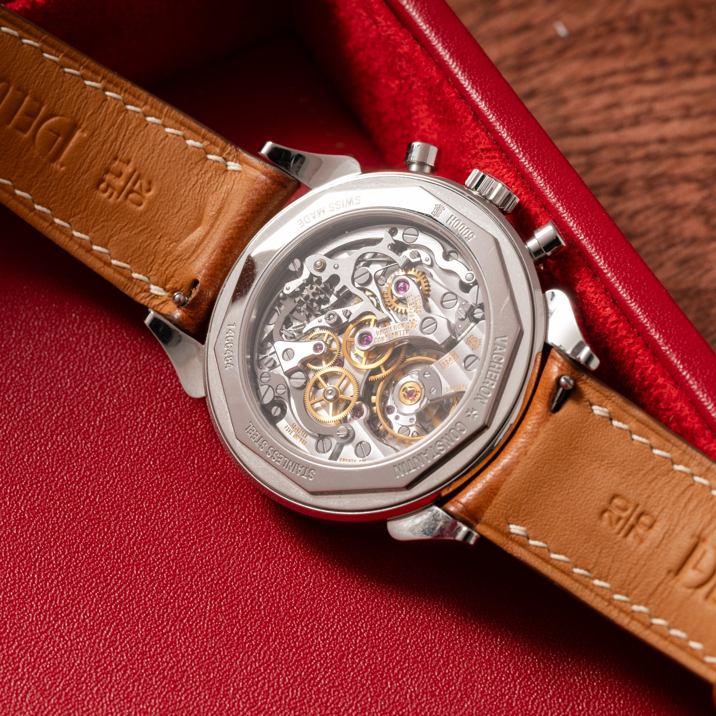 The Vacheron Constantin Historiques Cornes De Vache Chronograph, featuring a brown leather strap and an intricate exhibition caseback, is displayed in a red case.