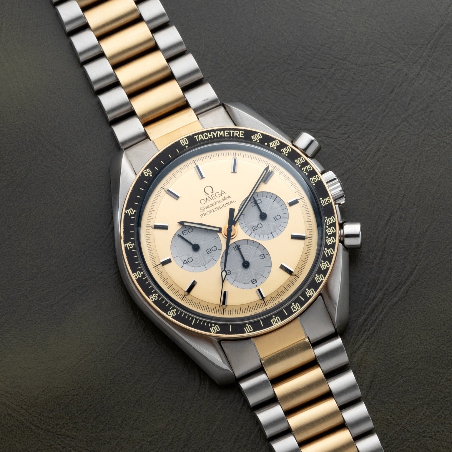 The OMEGA Speedmaster Professional Two-Tone features a striking gold and silver bracelet, showcased elegantly on a dark leather surface.