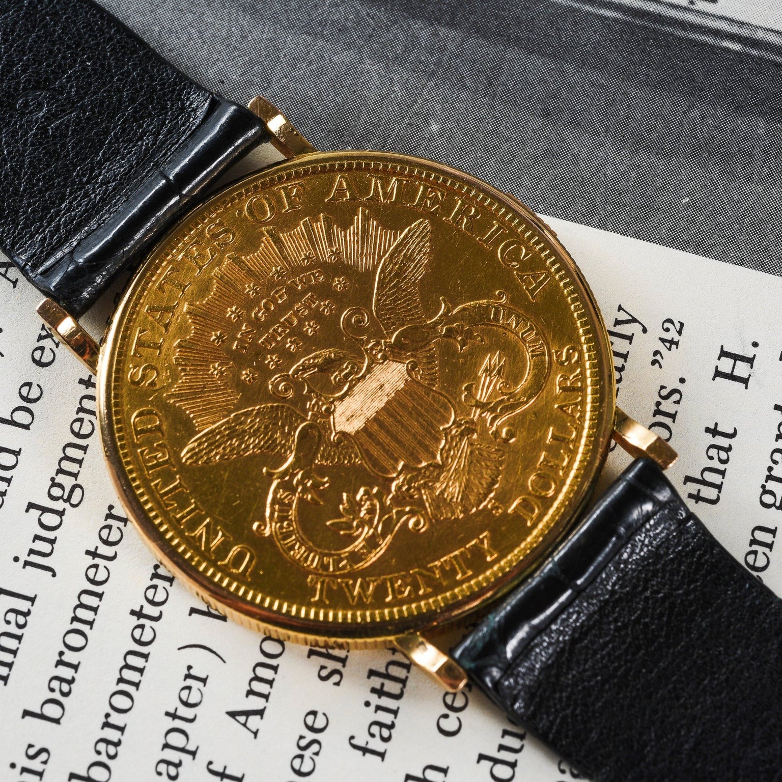 The Piaget 1877 Twenty Dollar Coin Watch, featuring a US eagle emblem on its gold face, is displayed atop an open book.
