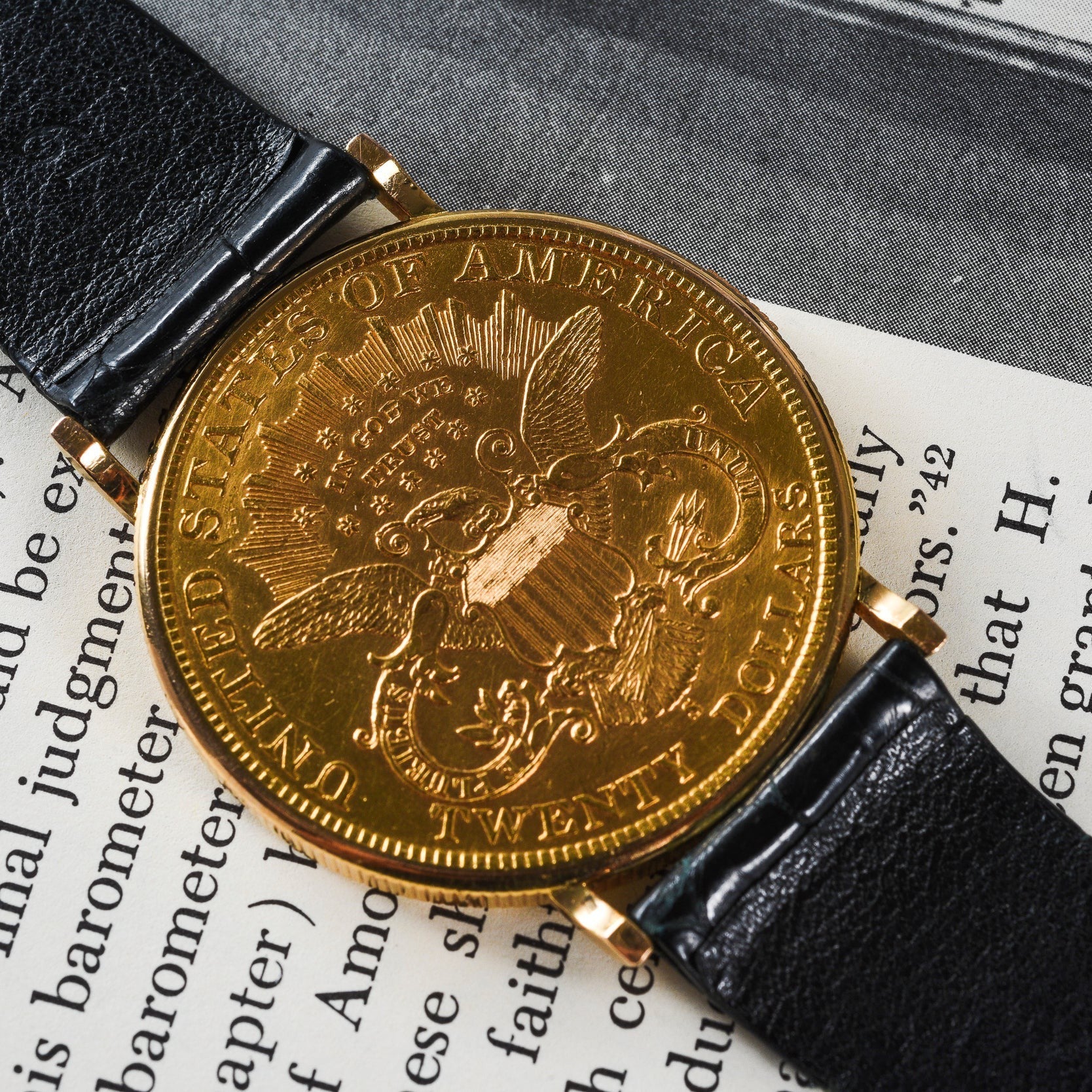 The Piaget 1877 Twenty Dollar Coin Watch, featuring a US eagle emblem on its gold face, is displayed atop an open book.