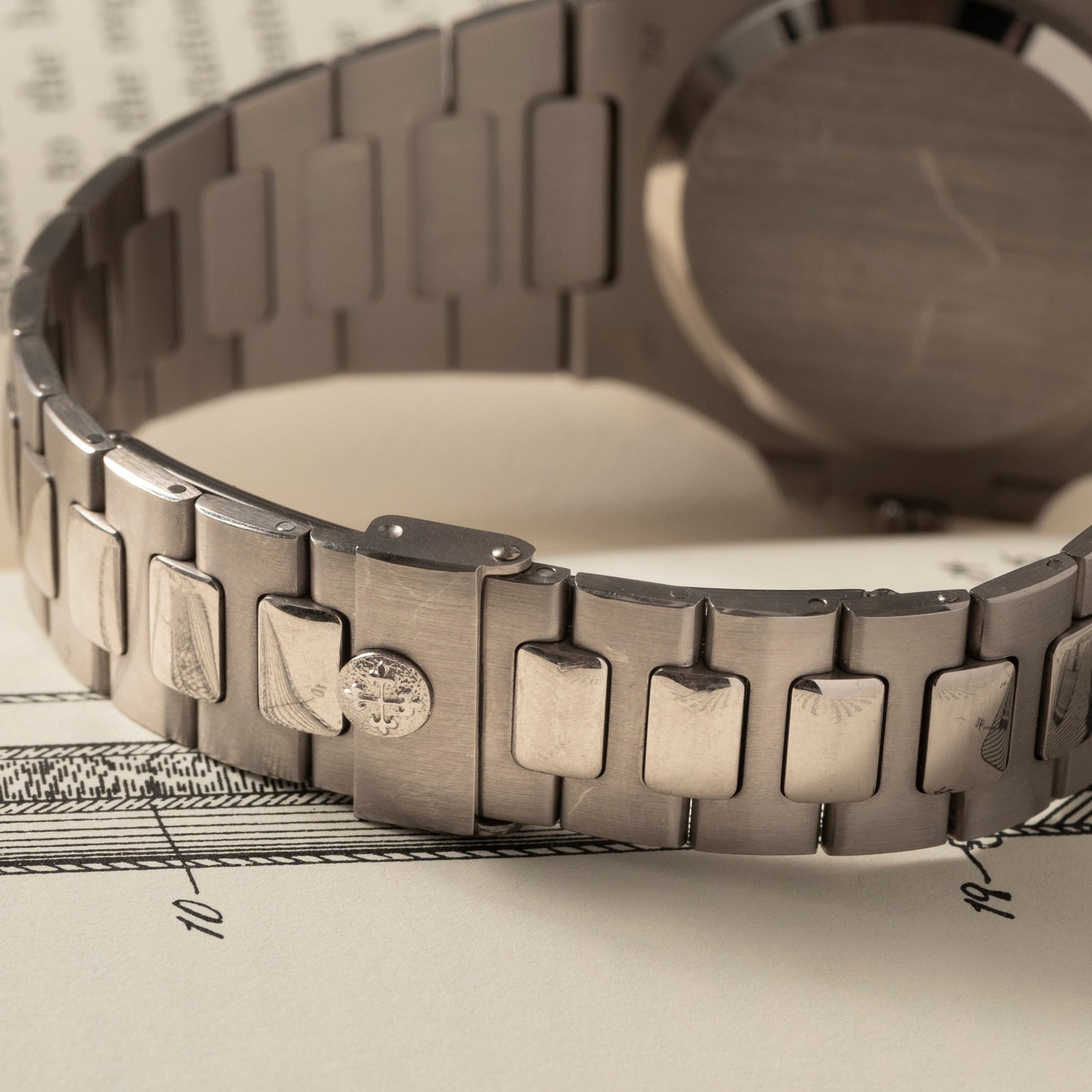 Close-up of a Patek Philippe Nautilus metal watch bracelet with visible scratches, resting on a sheet of paper with printed numbers.