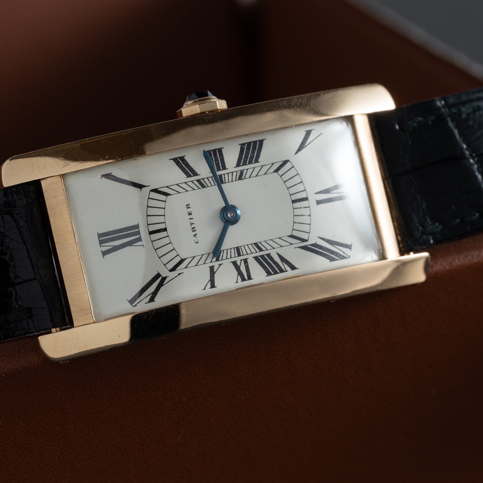 The Cartier Tank Cintrée Jumbo is a rectangular gold watch featuring a white face with black Roman numerals and a black leather strap.