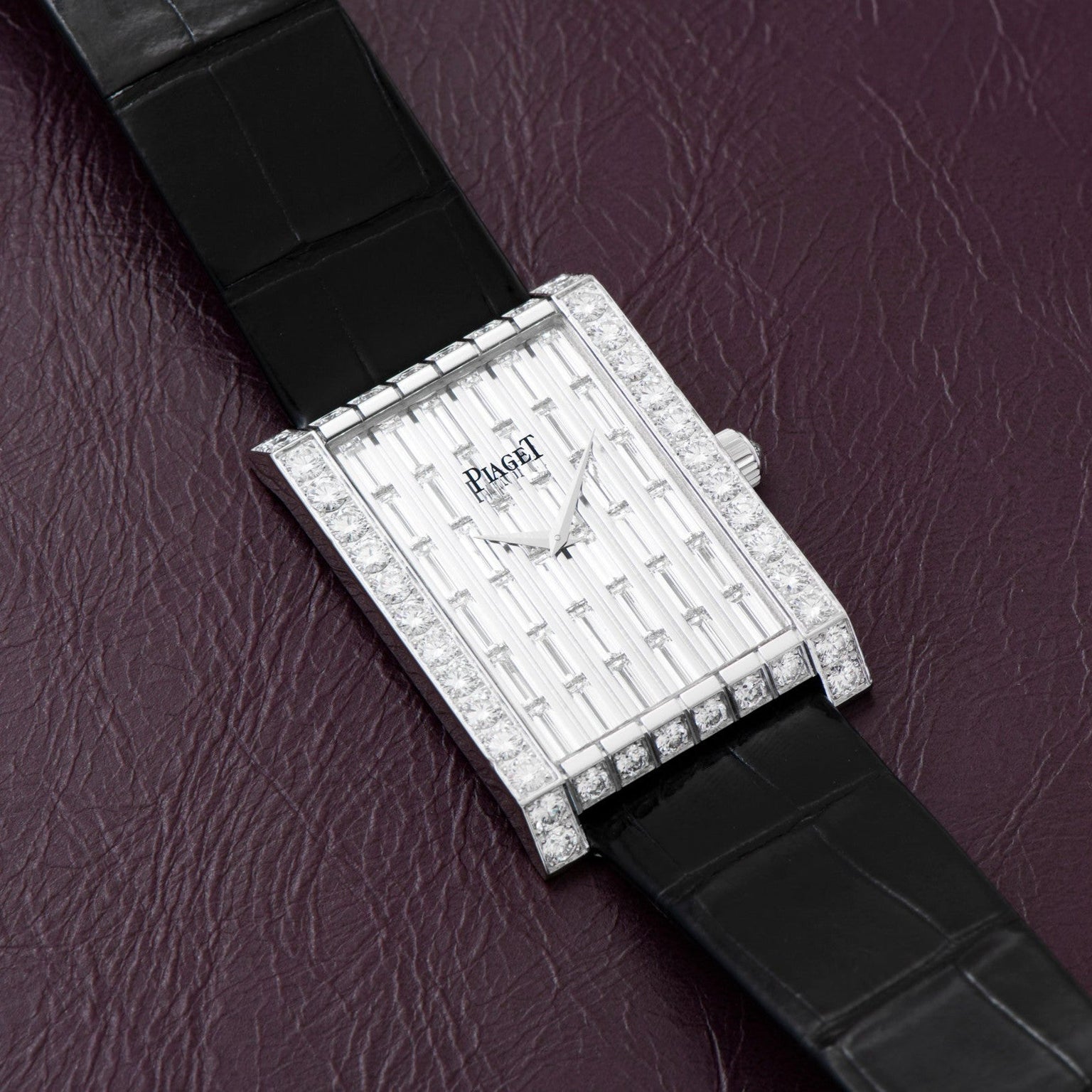 Piaget Limelight Baguette Diamond Dress Watch with black leather strap displayed on a textured burgundy surface.