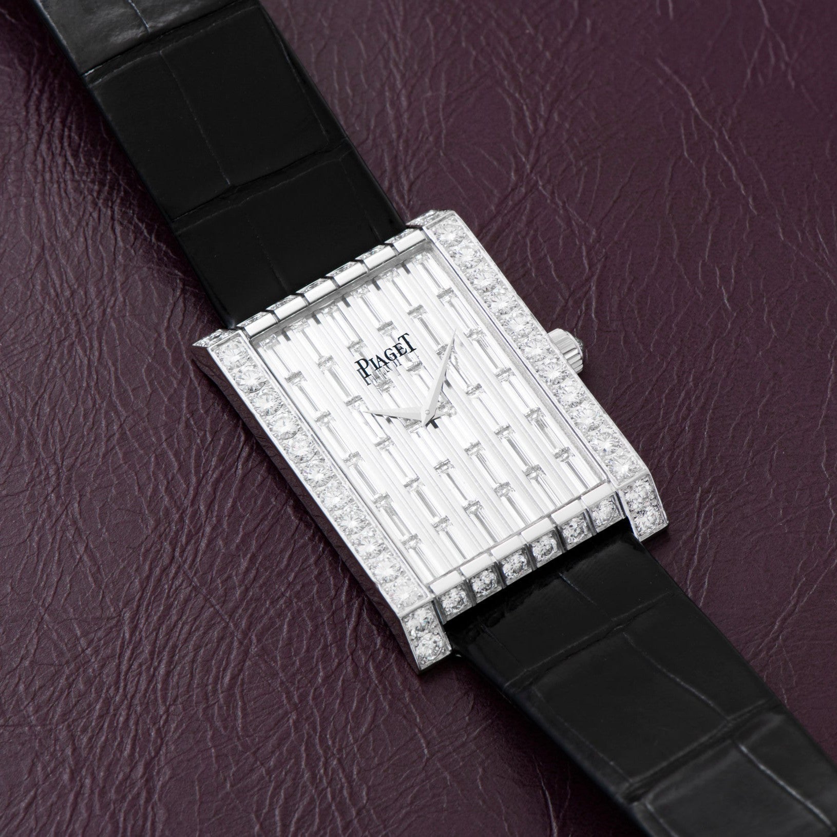 Piaget Limelight Baguette Diamond Dress Watch with black leather strap displayed on a textured burgundy surface.