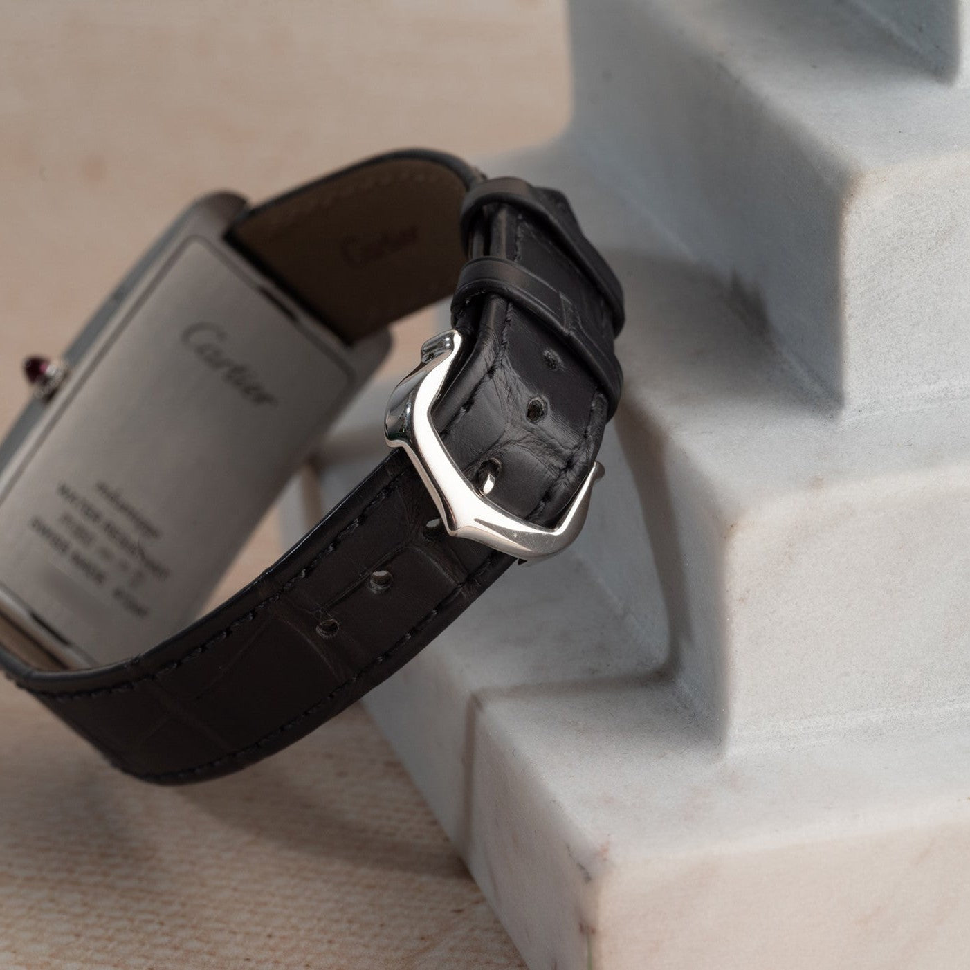 Close-up of the Cartier Tank Cintrée Piece Unique featuring a black leather strap and silver buckle on a white marble surface.