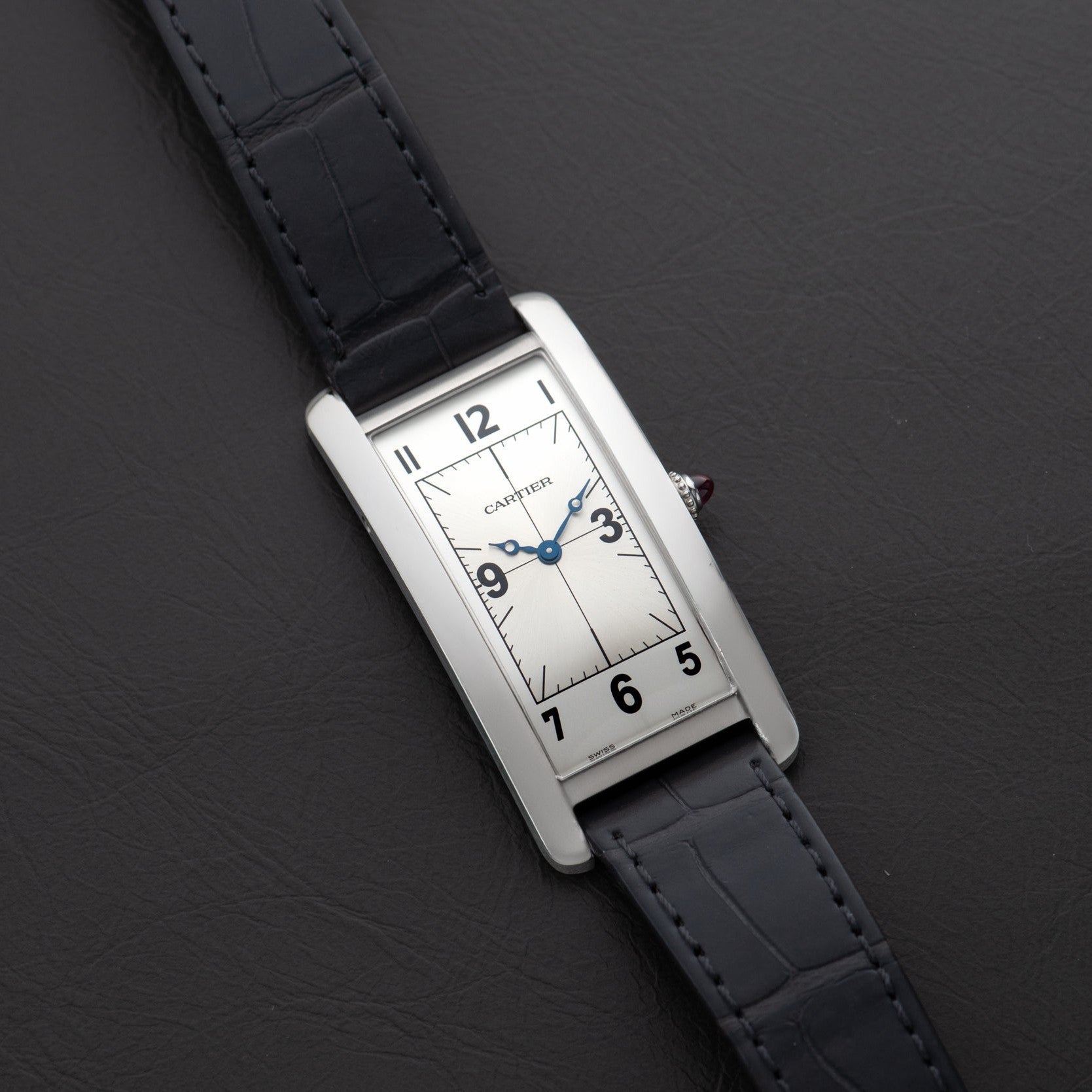 A Cartier Tank Cintrée Piece Unique rectangular wristwatch with a black leather strap rests on a dark leather surface.