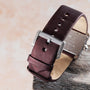 Close-up of a maroon Cartier Tank Divan watch strap with a silver buckle on a light textured background.