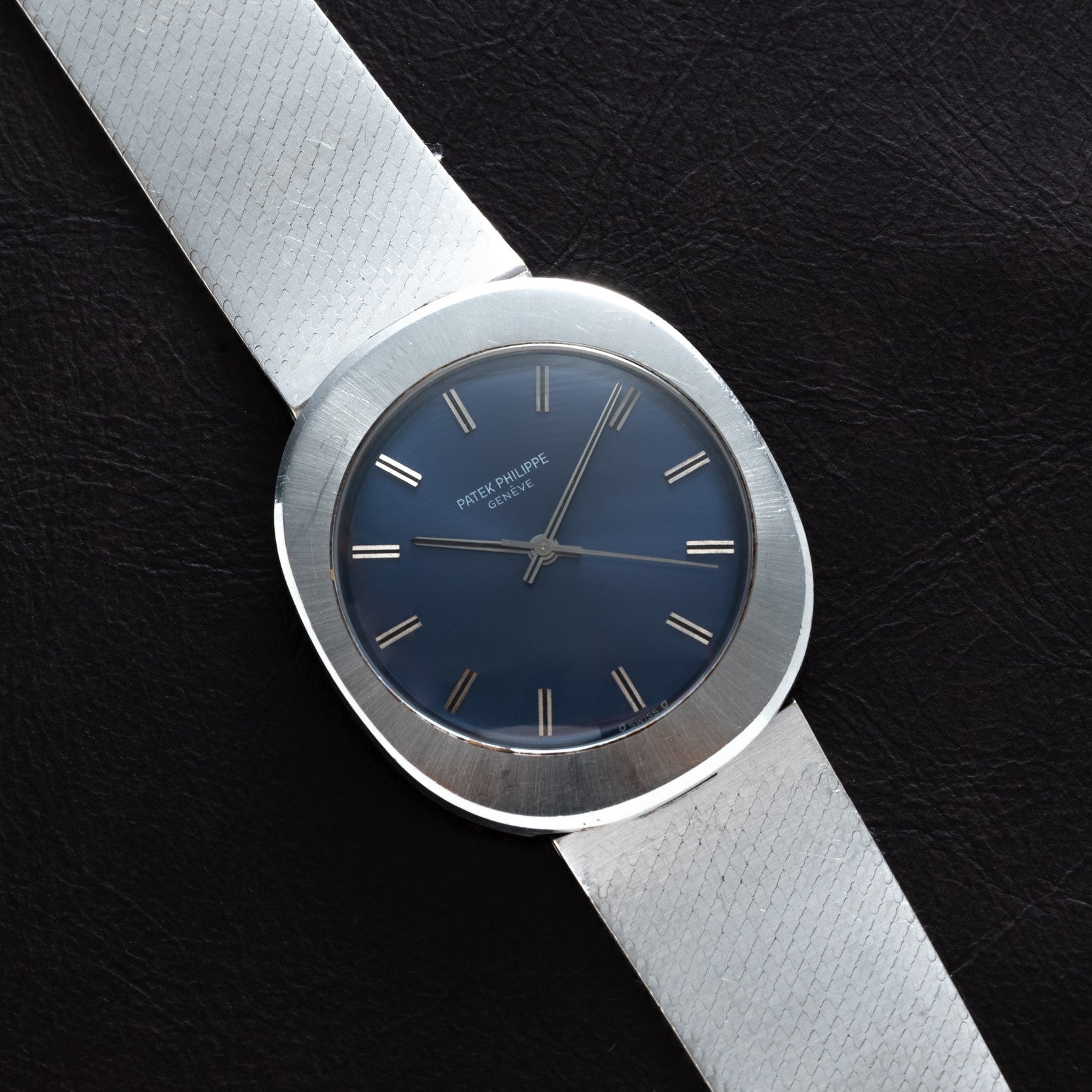 The Patek Philippe Dress Watch UFO features a silver band and blue face, elegantly displayed on a dark textured surface.